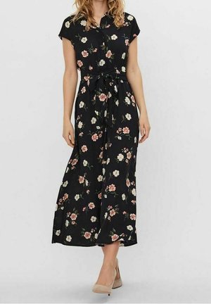 Musta midi-mekko, jossa on vaaleanpunainen ja valkoinen kukkakuosi, lyhyet hihat, napitettu etuosa ja vyötärökaitale, yhdistetty beigeihin korkokenkiin.