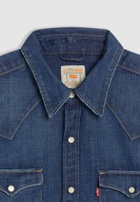Chemise en denim bleu foncé Levi's avec col pointu, boutons-pression, poches avant avec rabats et étiquette de marque visible à l'intérieur du col.