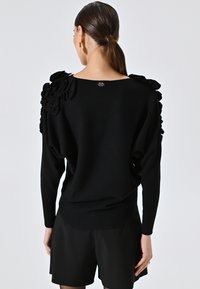 Maglione nero con rouches testurizzate sulle spalle, un ampio scollo e una silhouette aderente. Realizzato in morbido tessuto a maglia.