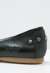 Czarne skórzane płaskie buty z teksturowanym panelem pięty, ozdobnymi ćwiekami i haftowanym logo. Okrągły czubek i elastyczna podeszwa.