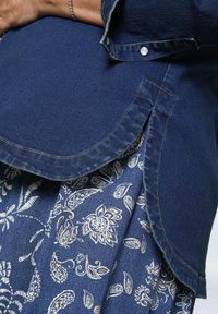 Denim shirt with a curved hem, button detail, paired with a patterned skirt featuring blue and white paisley designs. Textured fabric.