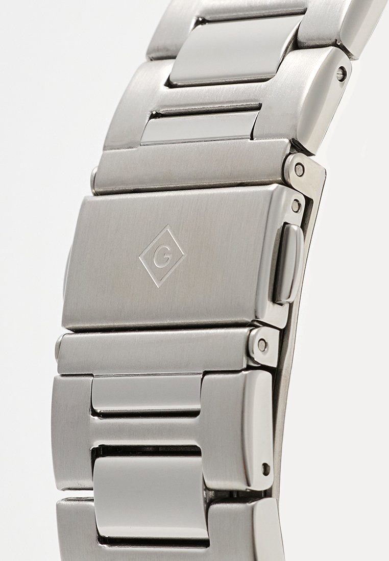 Bracelet en acier inoxydable argenté avec des maillons rectangulaires, textures brossées et polies, doté d'une fermeture avec un logo.