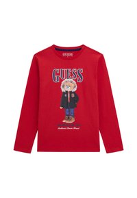 Crvena majica dugih rukava s grafikom lika lavova u crnoj jakni i čizmama. Na prednjem dijelu istaknuto piše "GUESS".