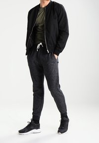 Black bomber jacket over an olive green t-shirt, paired with dark grey joggers and black sneakers. Slim fit, elastic cuffs, and drawstring waist.