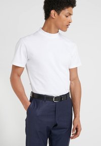 T-shirt bianca a maniche corte con colletto alto, abbinata a pantaloni a quadri blu navy e una cintura in pelle nera con fibbia argentata.