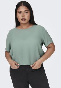 Top verde chiaro a maniche corte con scollatura rotonda e vestibilità morbida. Tessuto testurizzato, abbinato a jeans neri aderenti.