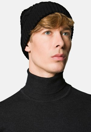 Czarna czapka typu beanie wykonana z dzianiny, z prążkowanym wzorem. Nosi się ją z czarnym golfem, który ma gładką teksturę.