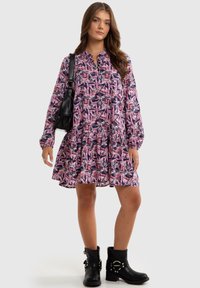 Long-sleeve dress with pink and purple leaf pattern, buttoned neckline, flared skirt, and black combat boots. Black handbag accent.