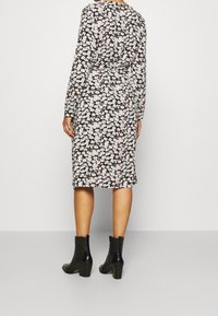 Blommig klänning med långa ärmar, svart bakgrund, vita och rosa blommor, åtsittande midja, knä-längd, kombinerad med svarta ankelskor.