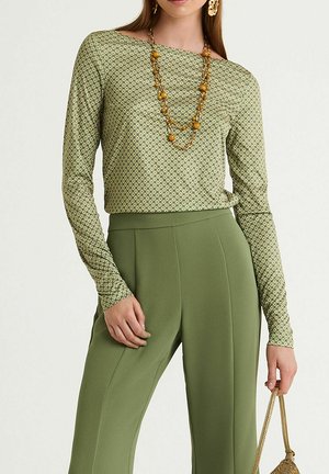 Maglia verde a maniche lunghe con motivo geometrico, abbinata a pantaloni verdi a vita alta. Accessoriata con una lunga collana multicolore.