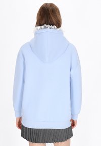 Sudadera azul claro de gran tamaño con una capucha espaciosa y un cuello blanco con volantes, combinada con una falda gris plisada. Textura suave y diseño casual.