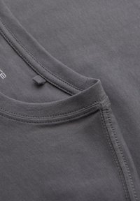 T-shirt in cotone grigio con scollatura arrotondata, cuciture visibili e un anello per l'etichetta. La texture del tessuto appare liscia e leggermente melangiata.