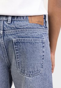 Τζιν παντελόνι από ανοιχτό μπλε denim με ελαφρώς ξεθωριασμένο πλύσιμο, διαθέτει δύο πίσω τσέπες, καφέ δερμάτινο έμπλαστρο στη ζώνη μέσης και ραμμένες λεπτομέρειες.