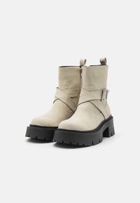 Beige potītes zābaki, kas izgatavoti no gludas ādas, ar sānu rāvējslēdzēju, sprādzes akcentu un masīvu melnu gumijas zoli ar rakstu.