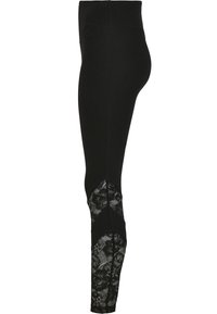 Leggings noirs avec une taille haute et des panneaux latéraux en dentelle arborant des motifs floraux sur le bas de la jambe. Texture lisse, design ajusté.