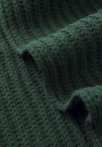 Dark green knitted fabric with a textured, ribbed pattern. The cloth appears soft and slightly fuzzy, featuring uneven folds.