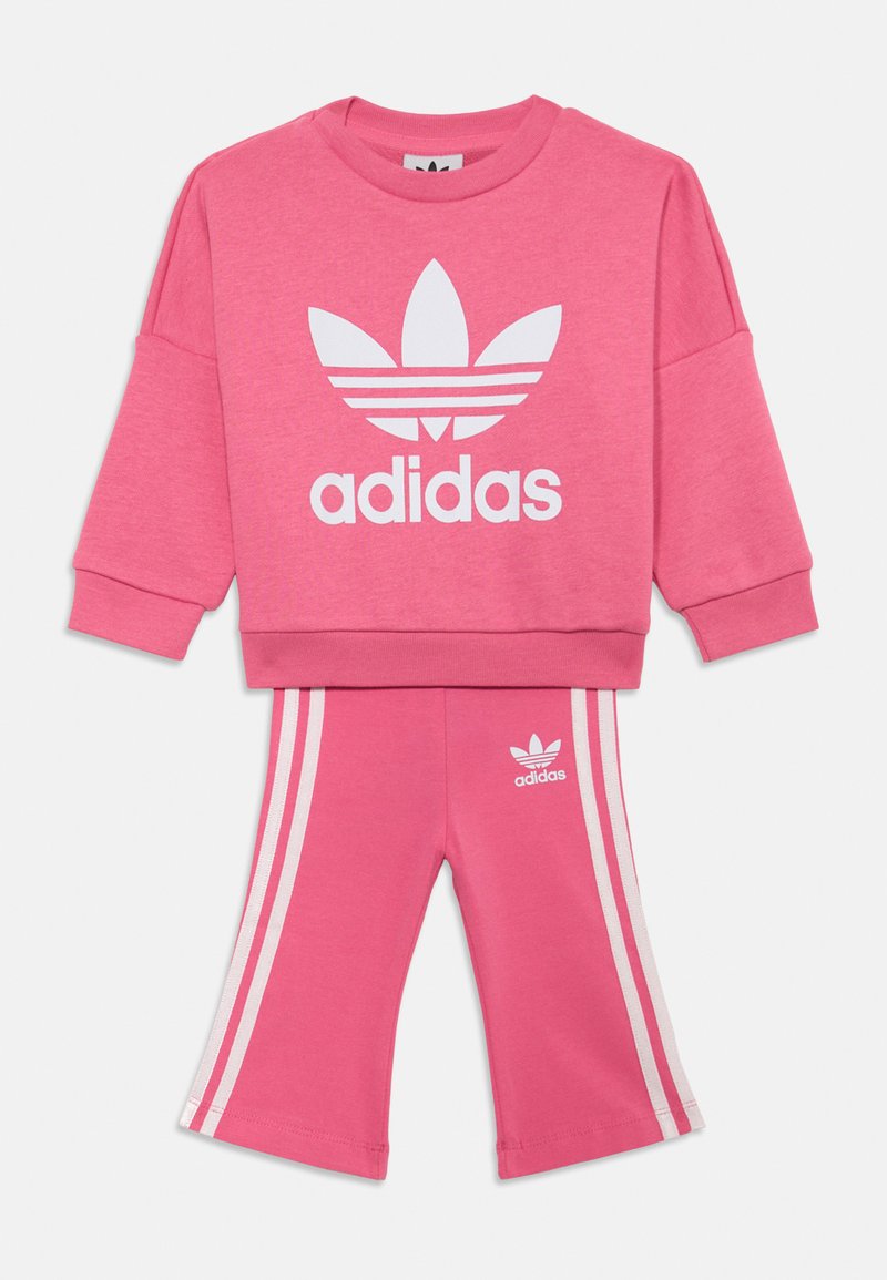 Ensemble de sweat-shirt rose et de pantalons assortis, avec le logo Adidas blanc et trois bandes blanches sur les côtés des pantalons, fabriqué en tissu doux et texturé.