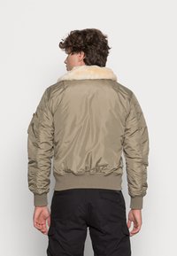 Chaqueta bomber verde oliva con cuello de piel, dobladillo y puños acanalados, bolsillos laterales y una textura suave y brillante.