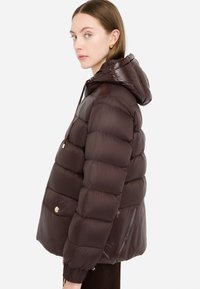 Giacca a vento marrone con cappuccio, caratterizzata da un design trapuntato, polsini elastici e dettagli in metallo dorato. Texture liscia e lucida.
