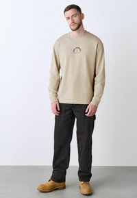 Beige langærmet skjorte med sort grafisk tekst, parret med mørke cargo bukser og brune sikkerhedssko, med lige snit og praktiske lommer.