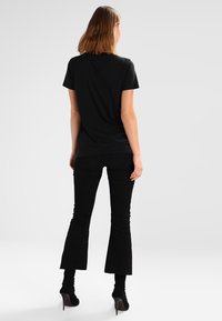 Svart kortärmad t-shirt i kombination med svarta kordflorsbyxor med utsvängda ben, som visar en åtsittande form och texturerad tyg, bärs med högklackade stövlar.