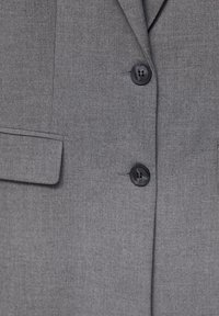 Blazer gris au tissu lisse, doté de deux boutons noirs, d'une poche sur le côté gauche et d'un col classique.