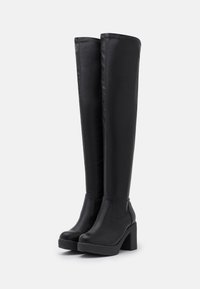 Botas negras hasta la rodilla hechas de cuero sintético con una textura suave, cuentan con un tacón grueso y un diseño minimalista, sin patrones ni acentos visibles.