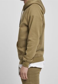 Olivově zelená mikina s kapucí má přední kapsu, žebrované manžety a lem. Vyrobena z texturované směsi bavlny.