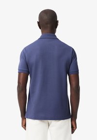 Polo di colore blu navy con una texture morbida, maniche corte e un colletto piccolo, visto da dietro, abbinato a pantaloni chiari.