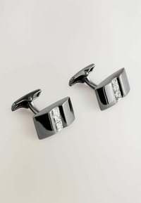 Schwarze Metallmanschettenknöpfe mit polierter Oberfläche, die eine horizontale Reihe von drei klaren Edelsteinen auf jedem Stück zeigen, rechteckiges Design.