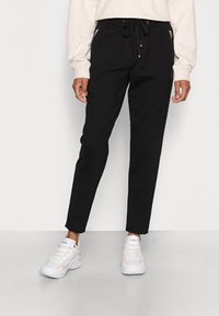 Zwarte joggers met een trekkoord in de taille, zijzakken met rits, taps toelopende pijpen en een zachte stof, gecombineerd met witte sneakers.