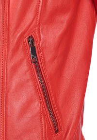 Röd läderjacka med en närbild av en dragkedjeficka. Har en jämn yta och metallisk dragkedjehårdvara.