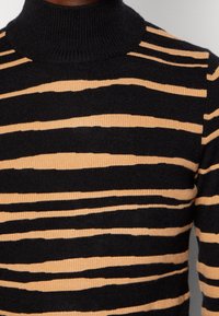 Pull noir avec des rayures beiges verticales, doté d'un col haut côtelé et d'un tissu texturé. Les rayures varient en largeur et en texture.