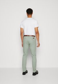 Witte kortemouwen t-shirt, lichtgroene slim-fit broek, bruine riem en zwarte schoenen. Glad materiaal, casual ontwerp, achteraanzicht.