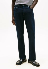 Jeans din denim de culoare albastră închisă, cu croială dreaptă, având buzunare frontale și sistem de închidere cu buton și fermoar. Textură netedă, cu detalii de cusătură discrete.