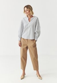 Stripet hvid og navy bluse med V-udskæring og puffede lange ærmer, parret med beige cropped bukser og nude højhælede mules.