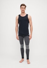 Schwarzes Tanktop und graue Leggings mit Mesh-Details, die ein körperbetontes Design und strukturierte Einsätze aufweisen. Das Tanktop hat ein Logo am Saum.
