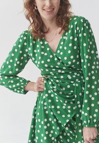 Grünes Wickelkleid mit Polka-Dots, langen Puffärmeln und geraffter Taille, mit V-Ausschnitt und fließendem Rock.