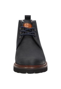 Botas de cuero negras hasta el tobillo con cordones azul marino, detalles en cuero marrón y suela de goma texturizada. Presentan una pestaña en el talón para facilitar su uso.