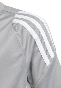 Maglia sportiva grigia caratterizzata da una texture liscia, tre strisce bianche lungo la spalla e un design leggermente strutturato per il comfort.