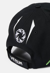 Zwarte pet met wit geborduurd logo en accenten, vervaardigd uit textuurstof. Verstelbare band met de tekst "VENUM" aan de achterkant.