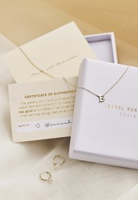 Gold necklace with "B" pendant and two gold hoop earrings with pearl accents, displayed with a certificate of authenticity on a neutral fabric.