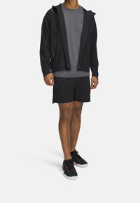 Černá mikina na zip přes šedé tričko, doplněná černými šortkami a černými sportovními botami s červenými detaily. Hladký materiál s volným střihem.