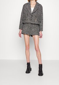 Textured, multicolored tweed jacket with oversized collar, double-breasted design, paired with matching shorts and black ankle boots.