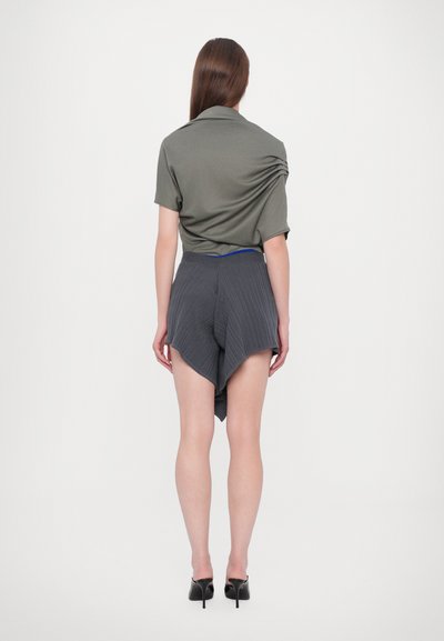 Oliven grøn kortærmet skjorte med draperet ryg, parret med grå ribbede shorts med asymmetrisk kant og en sort talje. Sorte hæle.