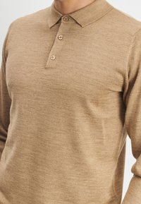 Tan langemouw polo shirt gemaakt van gestructureerde stof, met een klassieke kraag en drie bijpassende knopen bij de hals.