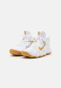 Baskets blanches au design épuré, arborant un logo Nike doré et une semelle speckled. Les lacets et les accents en nylon viennent parfaire l'ensemble.