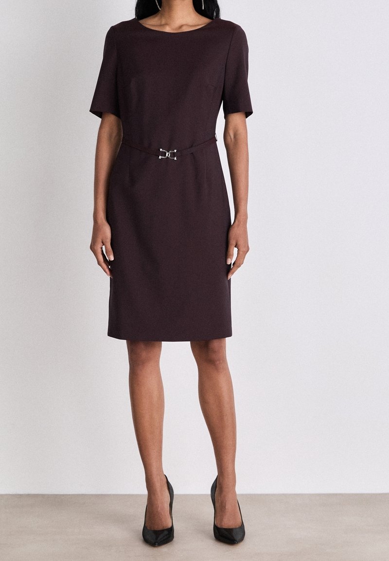 Burgundské šaty ke kolenům s krátkým rukávem, kulatým výstřihem a páskem v pase s detaily ve tvaru stříbrné spony. Hladká textilie.