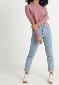 Top a maniche lunghe rosa chiaro a coste abbinato a jeans azzurri con risvolto. La modella indossa sneakers bianche con dettagli beige.