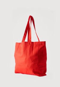 Κόκκινη υφασμάτινη τσάντα ώμου με διπλά λουριά, άδεια, τοποθετημένη σε απλό ανοιχτόχρωμο φόντο.